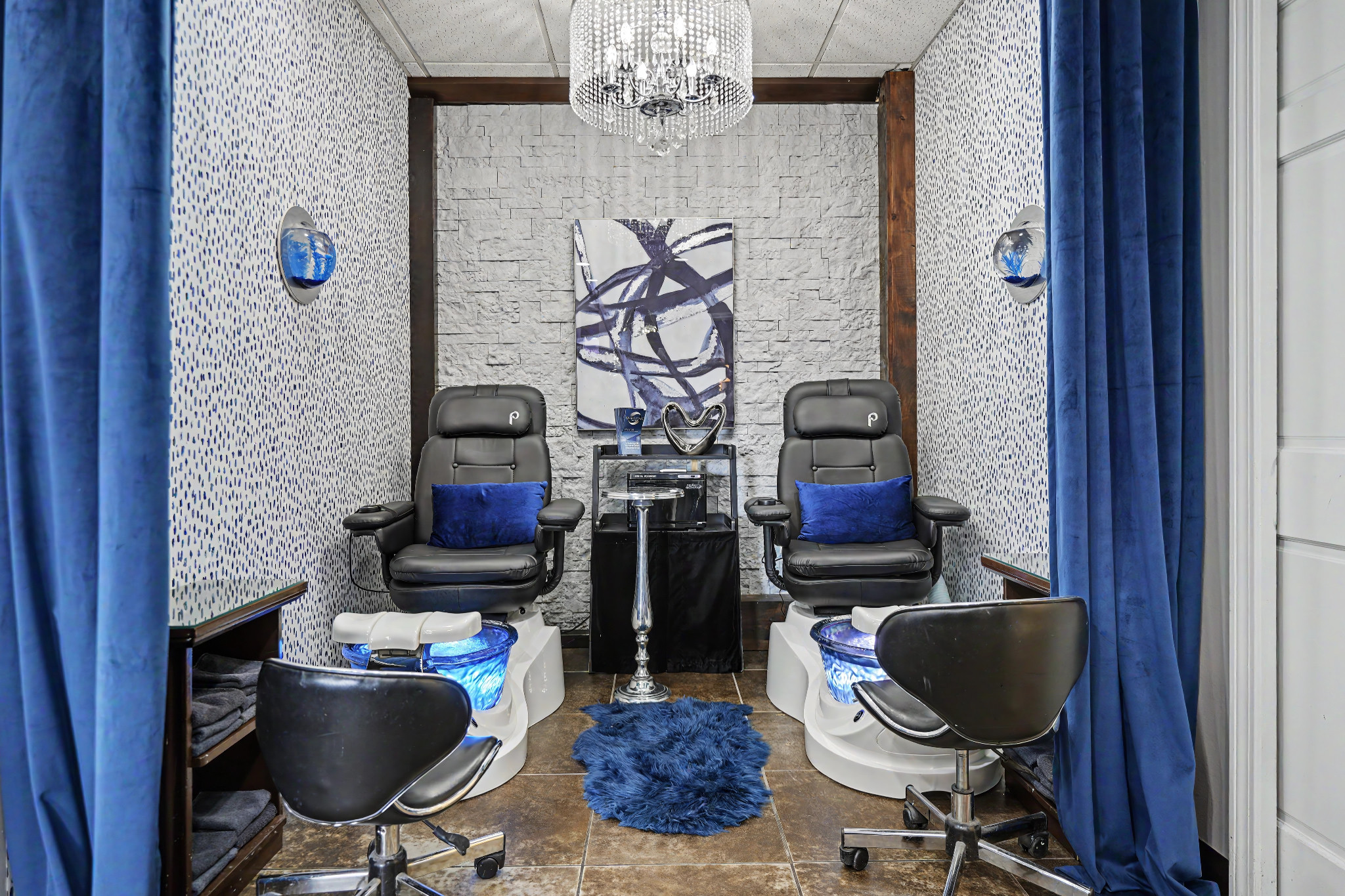 The Ovations pedicure room with two pedicure chairs, blue curtains and a crystal chandelier