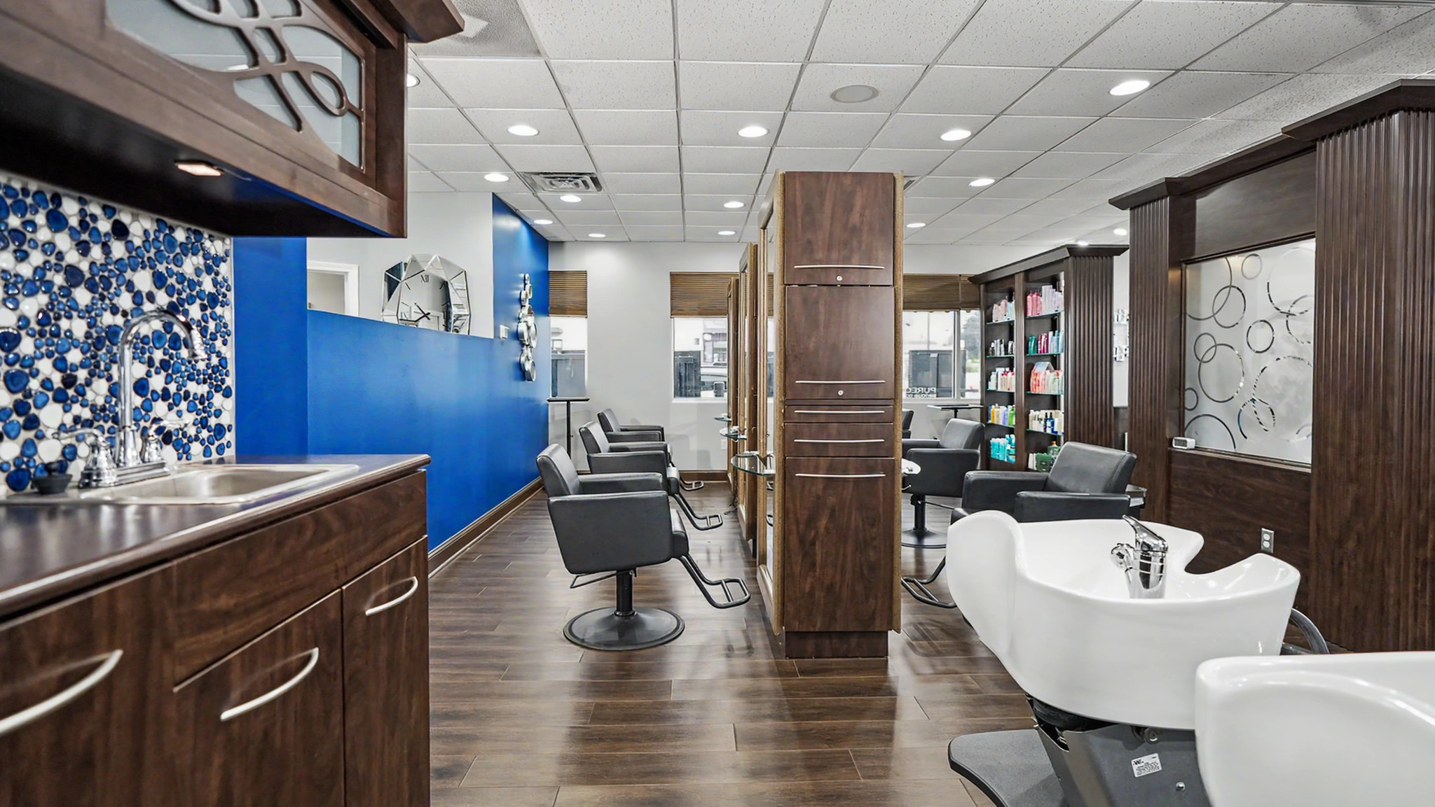 The Ovations styling floor, with black salon chairs, dark wood stations and blue accents